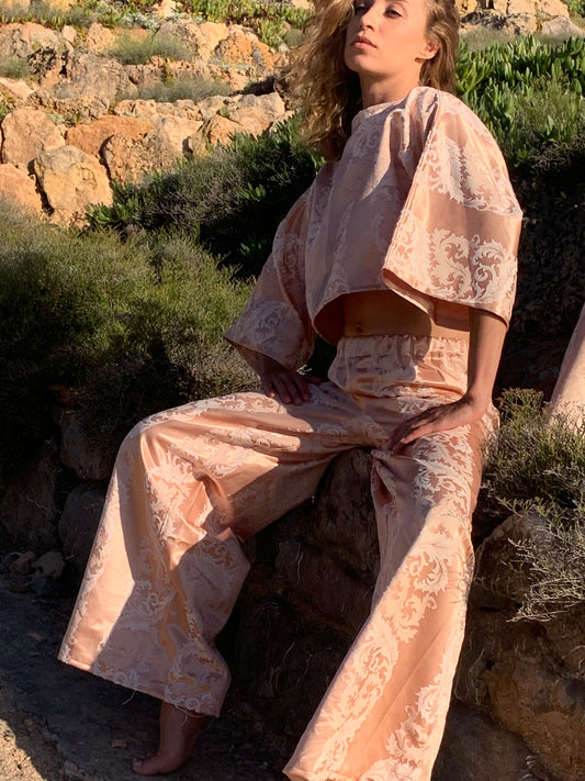 Handmade oversized pink brocade top with wide-leg trousers set, upcycled from vintage English fabric, styled outdoors in Ibiza.