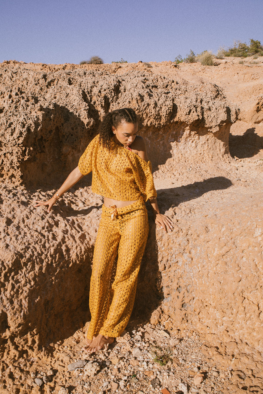 Model wearing mustard yellow 1970s open-weave crochet-style two-piece set, styled with a relaxed fit and ribbon-tie waist.
