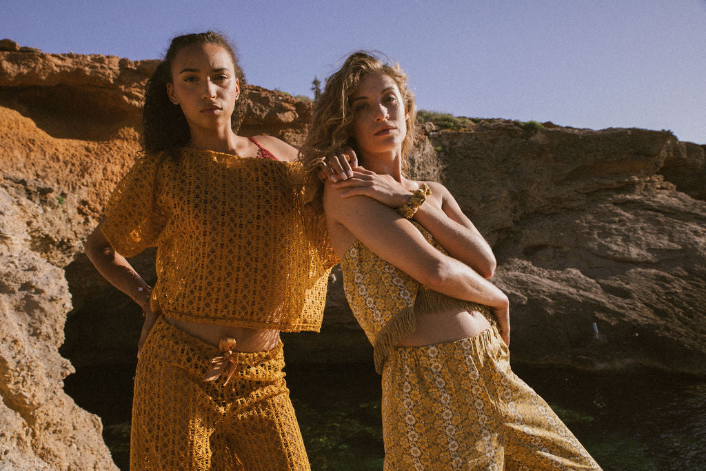 Model wearing mustard yellow 1970s open-weave crochet-style two-piece set, styled with a relaxed fit and ribbon-tie waist.
