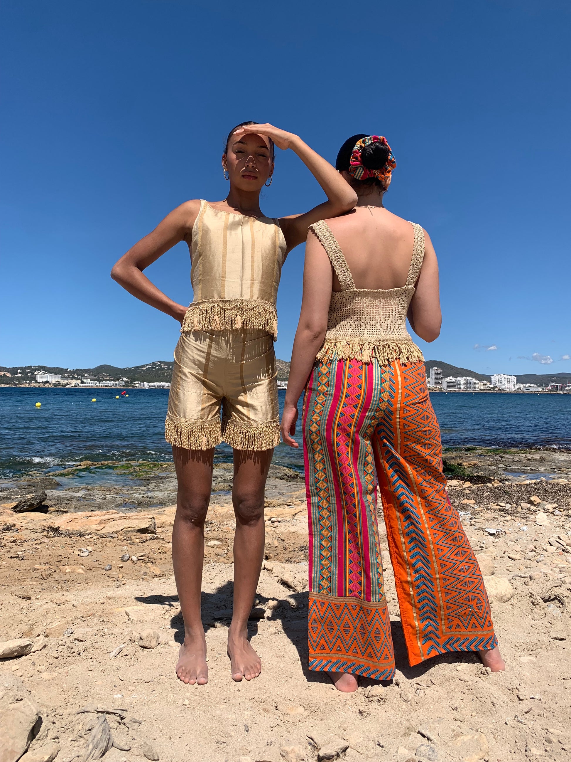 Model wearing gold vintage 1960s silk crochet crop top with tassel trim and wide straps, styled against natural Ibiza backdrop