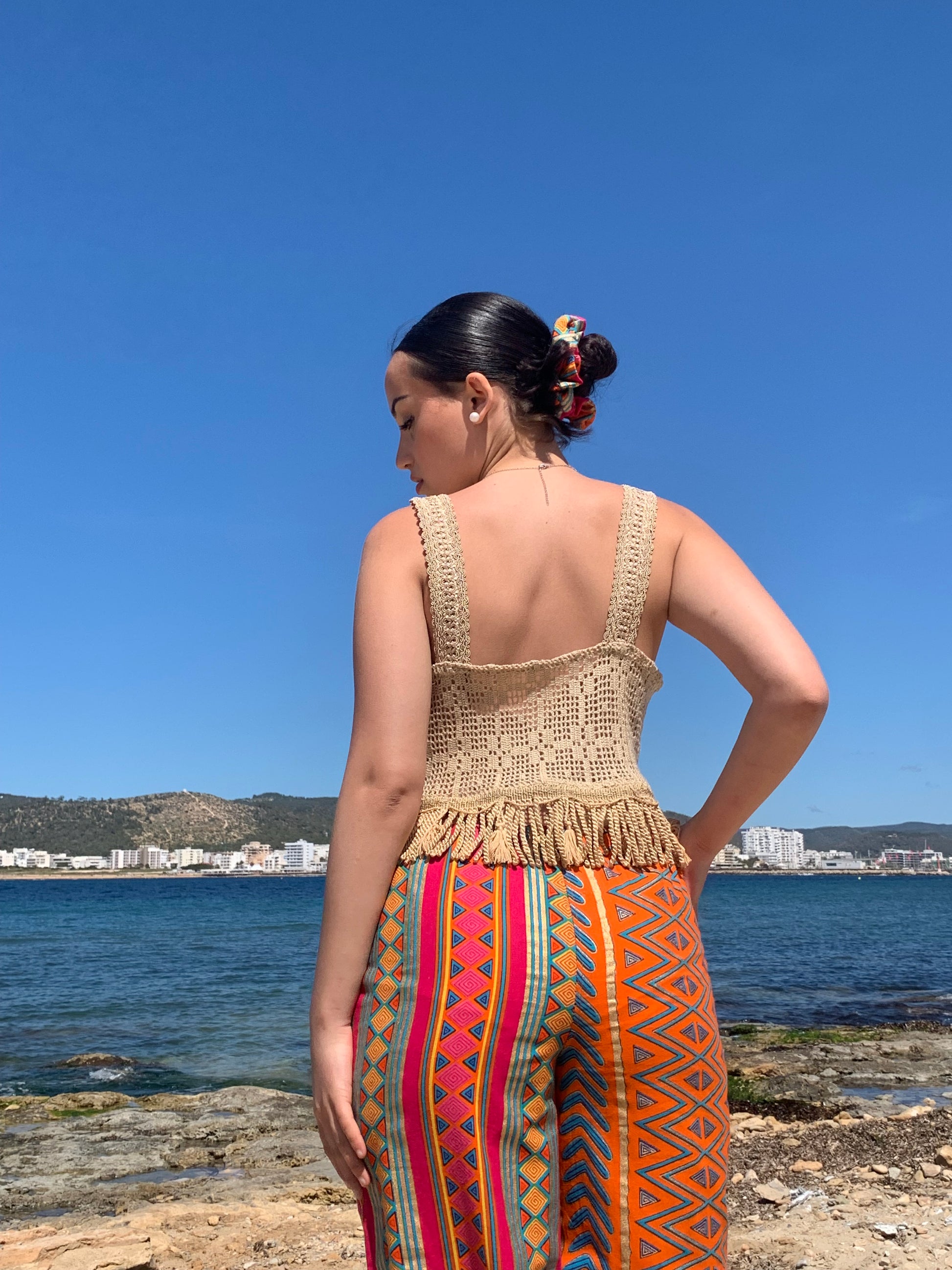 Model wearing gold vintage 1960s silk crochet crop top with tassel trim and wide straps, styled against natural Ibiza backdrop
